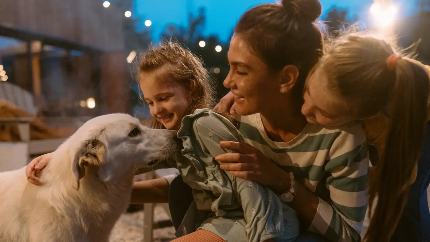 A mother and two girls lovingly greeting a white dog in a community program